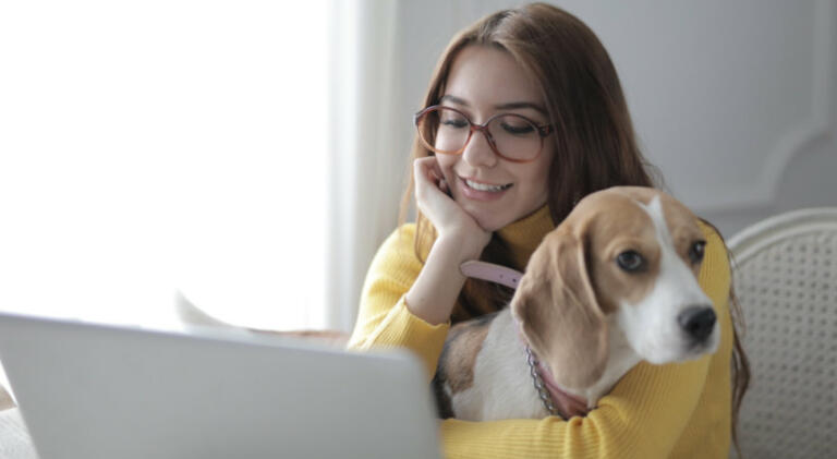 woman holds her dog on her lap while sitting in front of a laptop
