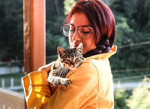 Woman with braided hair wearing a yellow sweatshirt and holding her cat